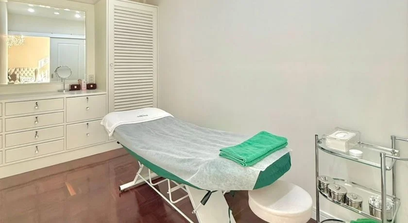 ห้องทรีตเมนต์ เตียงปูผ้าสะอาดพร้อมผ้าขนหนูสีเขียว ตู้ลิ้นชักสีขาว และกระจกแต่งหน้า